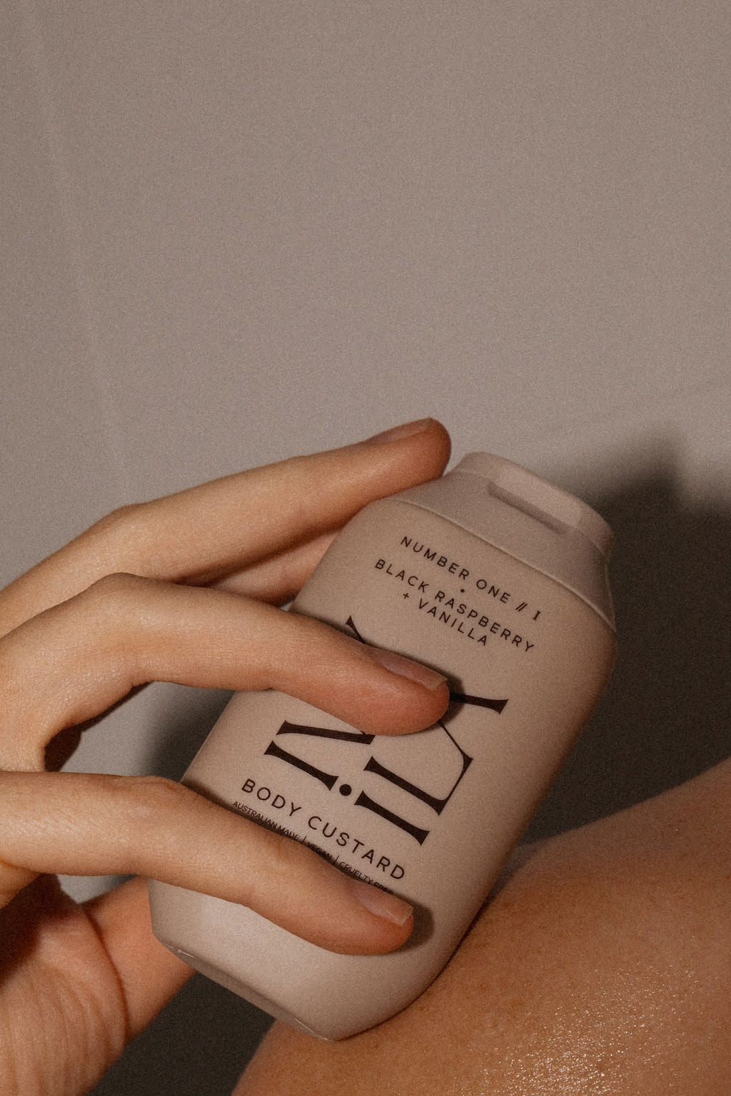 Hand holding a beige bottle labeled 'Body Custard' against a neutral background