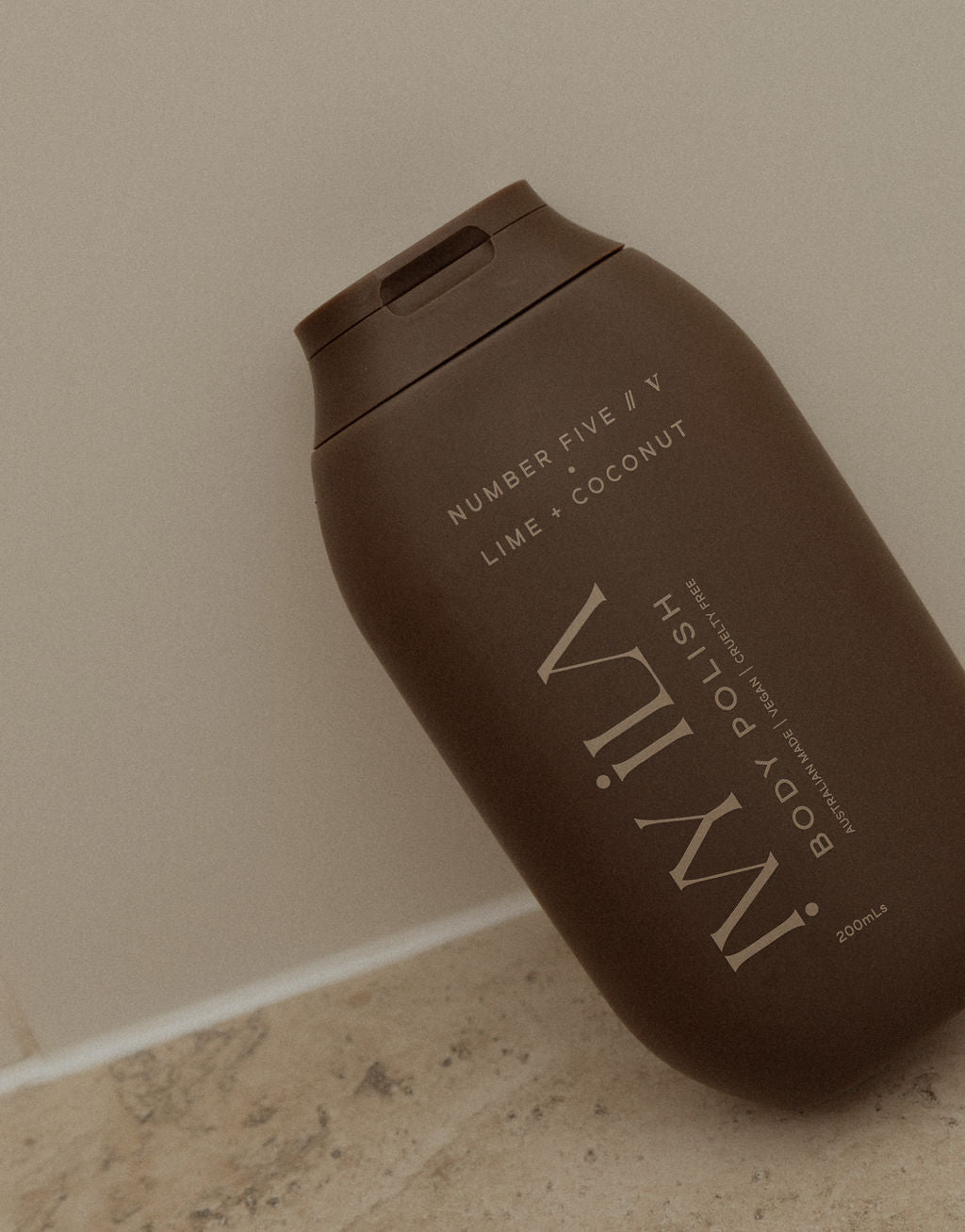 Brown bottle of IMWIL body polish on a beige floor against a beige wall