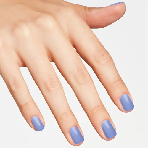 A close-up of a hand with neatly manicured nails painted in a soft periwinkle blue shade, set against a clean, light gray background.