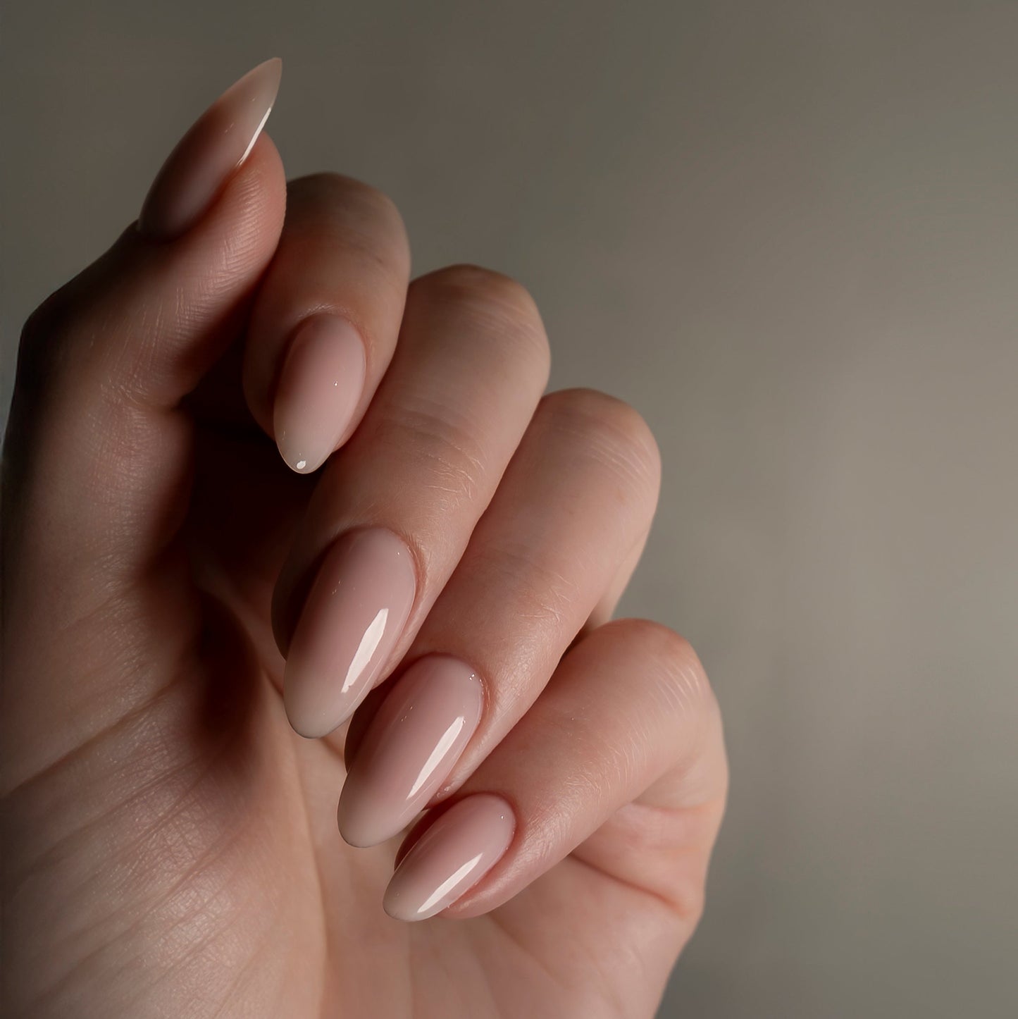 Close-up of a hand with beige nail polish on a neutral background