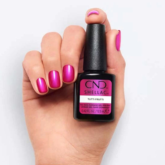 A hand with bright pink CND Shellac nails holds a bottle of CND Shellac nail polish against a clean white background.