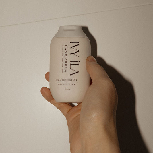 Hand holding a white bottle labeled 'Ily Ila' against a plain background hand cream