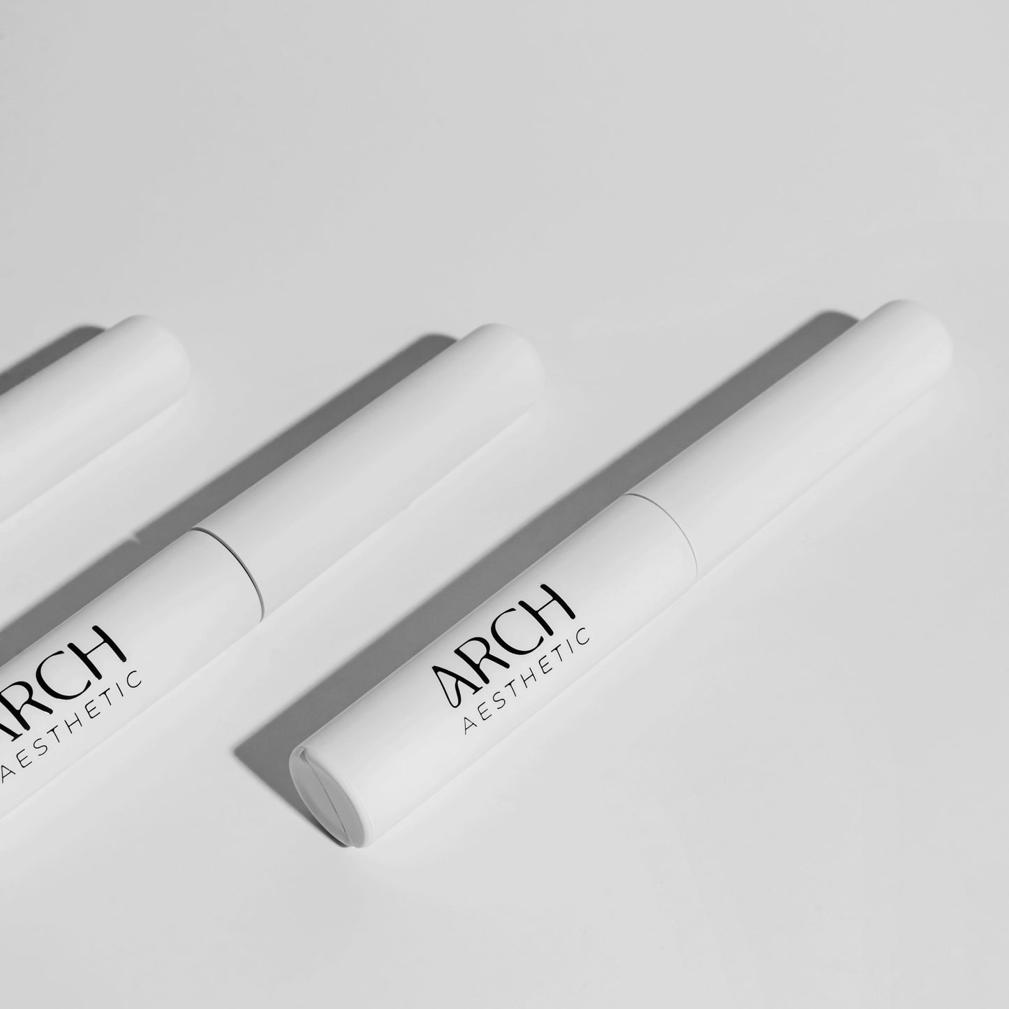 Two white cosmetic tubes with 'ARCH Aesthetics' branding on a light gray background