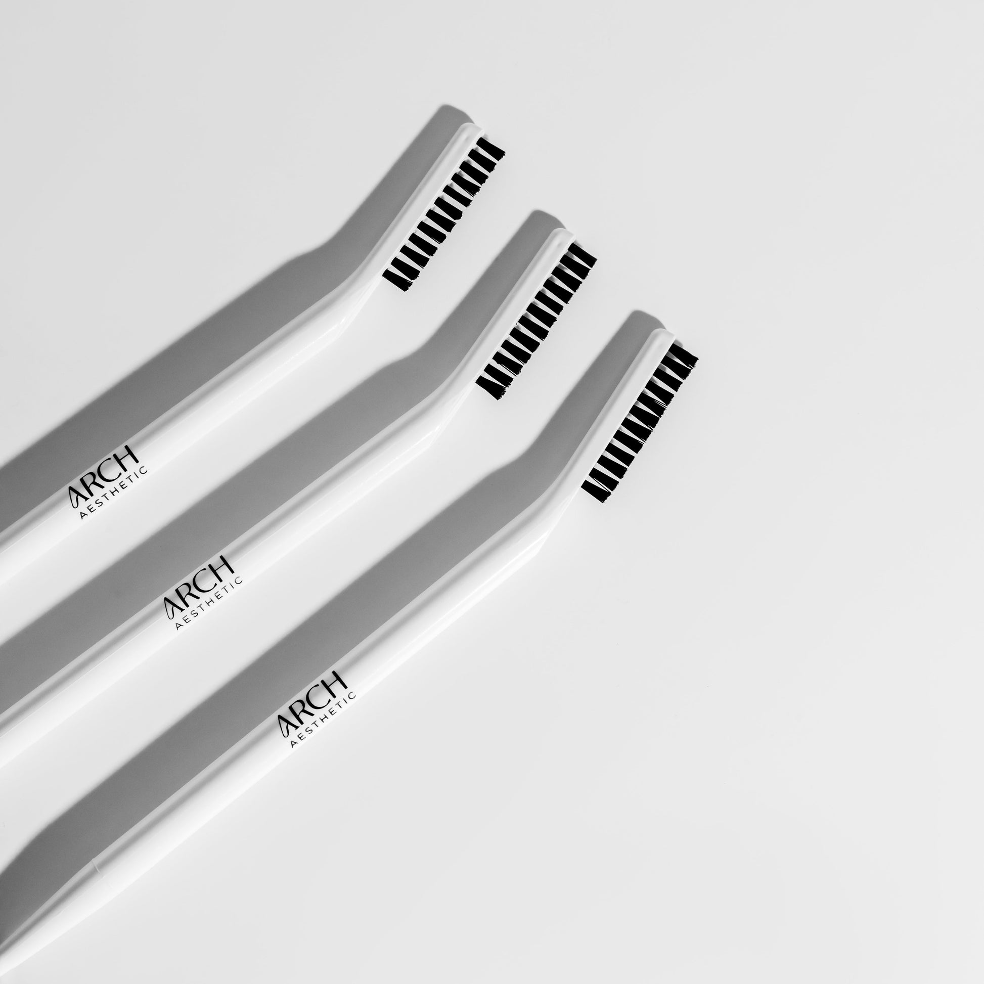 Three makeup brushes with black bristles on a light gray background