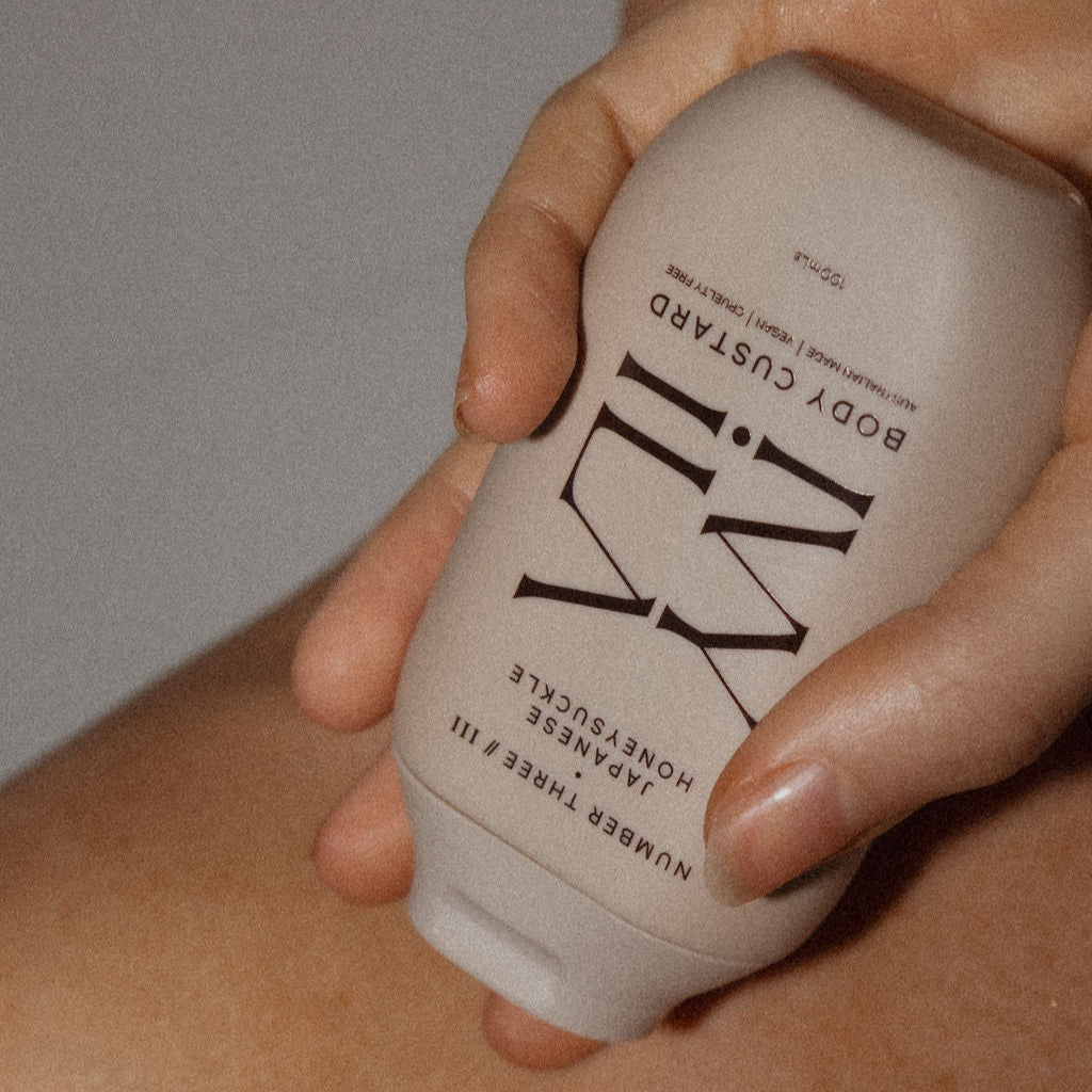 Hand holding a beige bottle labeled 'IVY ILA against a neutral background