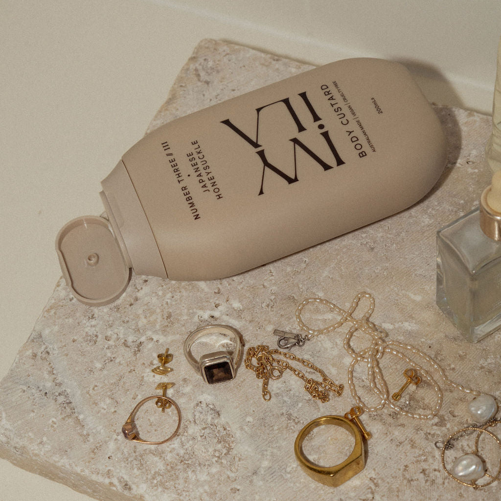 Body Custard lotion with 'Ivy Ila' branding on a stone surface with jewelry and a candle.