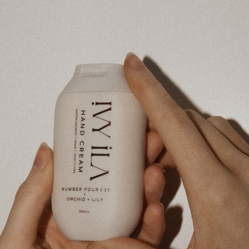 Hand holding a ivy ila hand cream container against a plain background