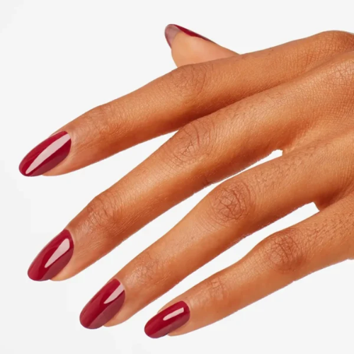A close-up of a hand with manicured fingernails painted in a glossy deep burgundy red, shown against a plain white background.