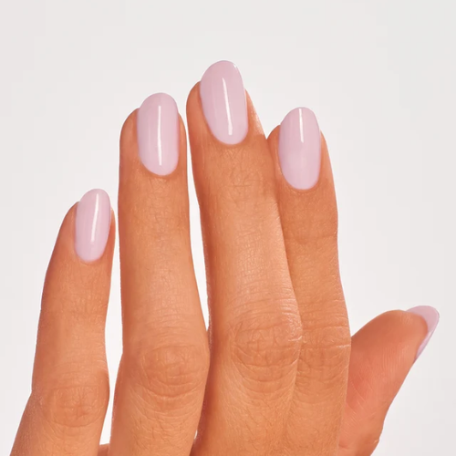 A close-up of a hand with neatly manicured nails painted in a glossy, pale pastel pink color, set against a clean, light gray background.