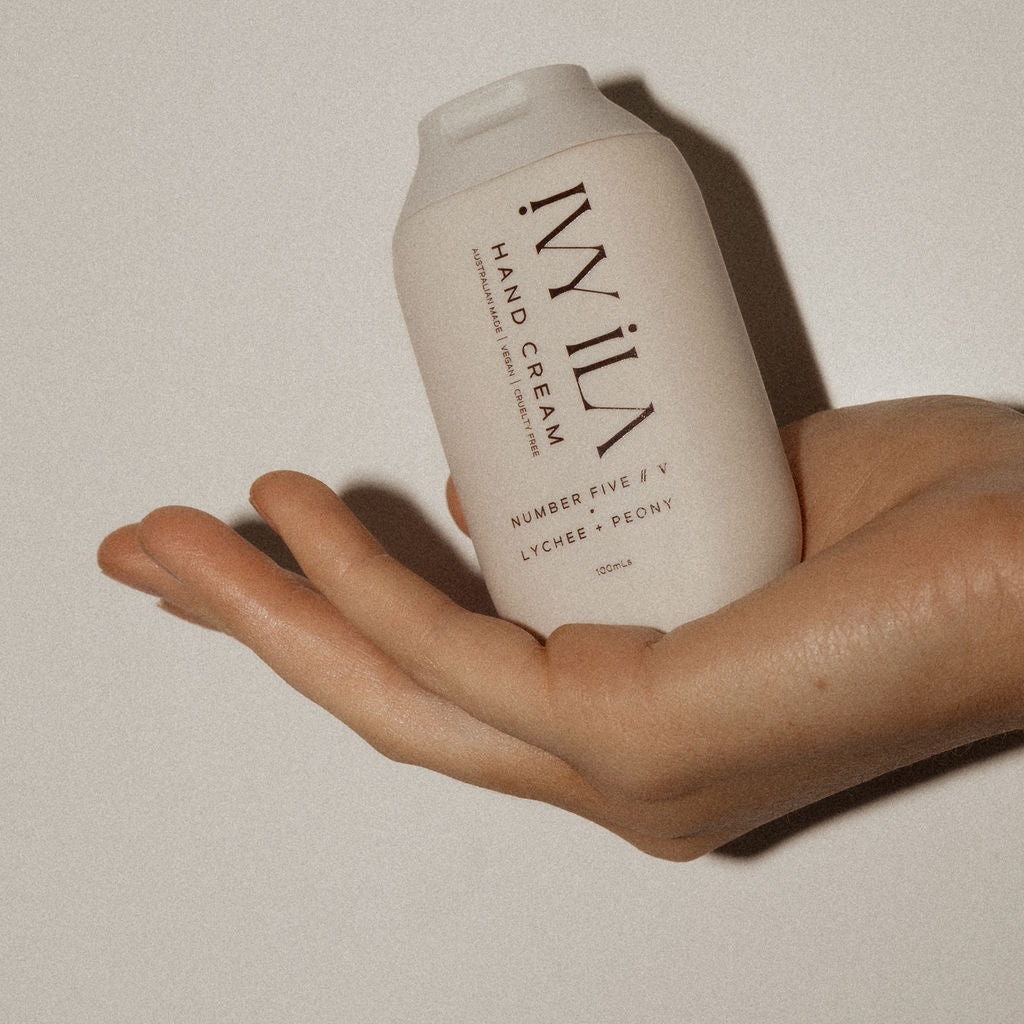 Hand holding a bottle of IVILA hand cream against a neutral background