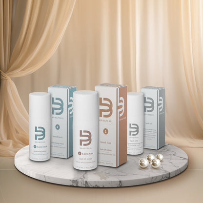 A set of lash lift products from Brik & Pearl arranged on a round marble pedestal. The products include Bond Flex, Bond Lock, and Lash Life in white bottles and boxes with teal, brown, and gray packaging, alongside three clear silicone bonding capsules on a beige draped fabric background.