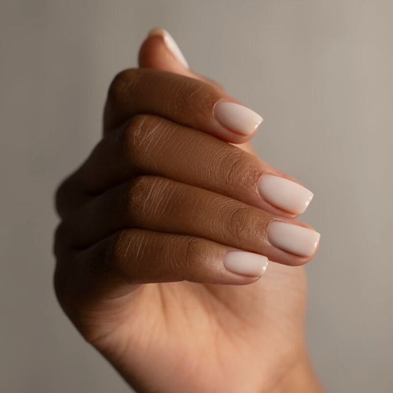 Close-up of a hand with light pink nail polish on a neutral background