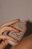 Hand holding a beige bottle labeled 'Body Custard' against a neutral background