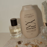 Body custard bottle with other skincare products and jewelry on a textured surface.