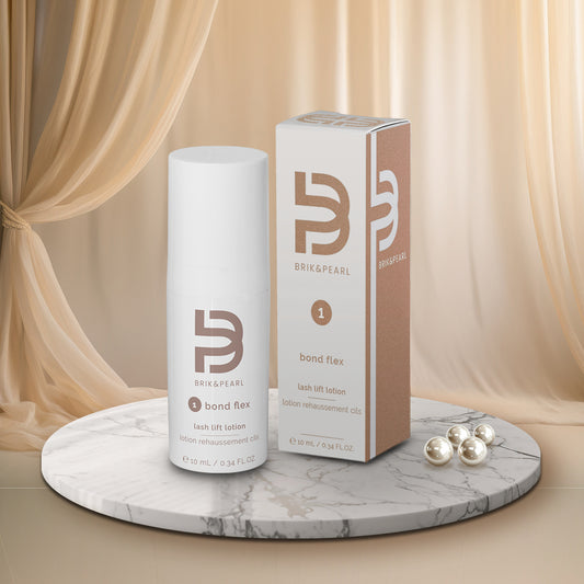 Brik & Pearl Bond Flex lash lift lotion shown as a white cylindrical bottle next to its brown and white packaging box, displayed on a round marble pedestal with decorative pearls and draped beige fabric in the background.