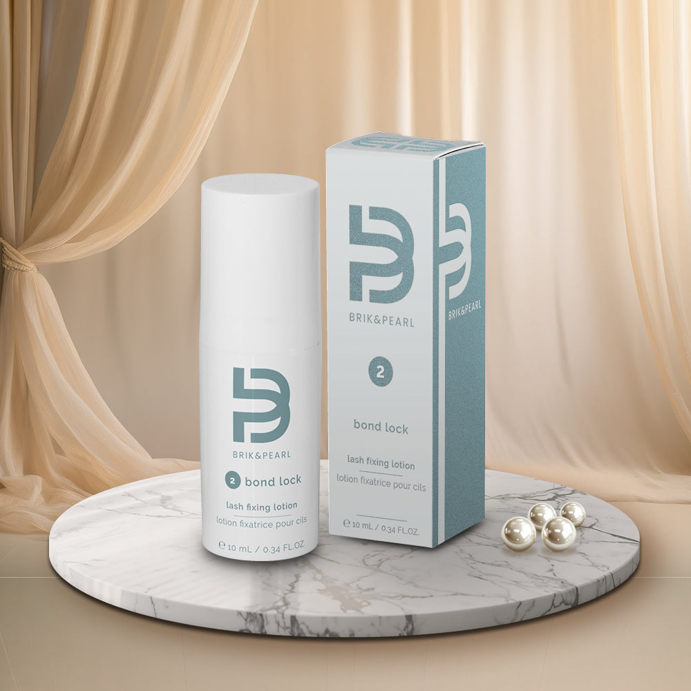 Bri&Pearl Bond Lock lash fixing lotion bottle and packaging box displayed on a round marble tray with pearl capsules, set against a backdrop of draped beige fabric.