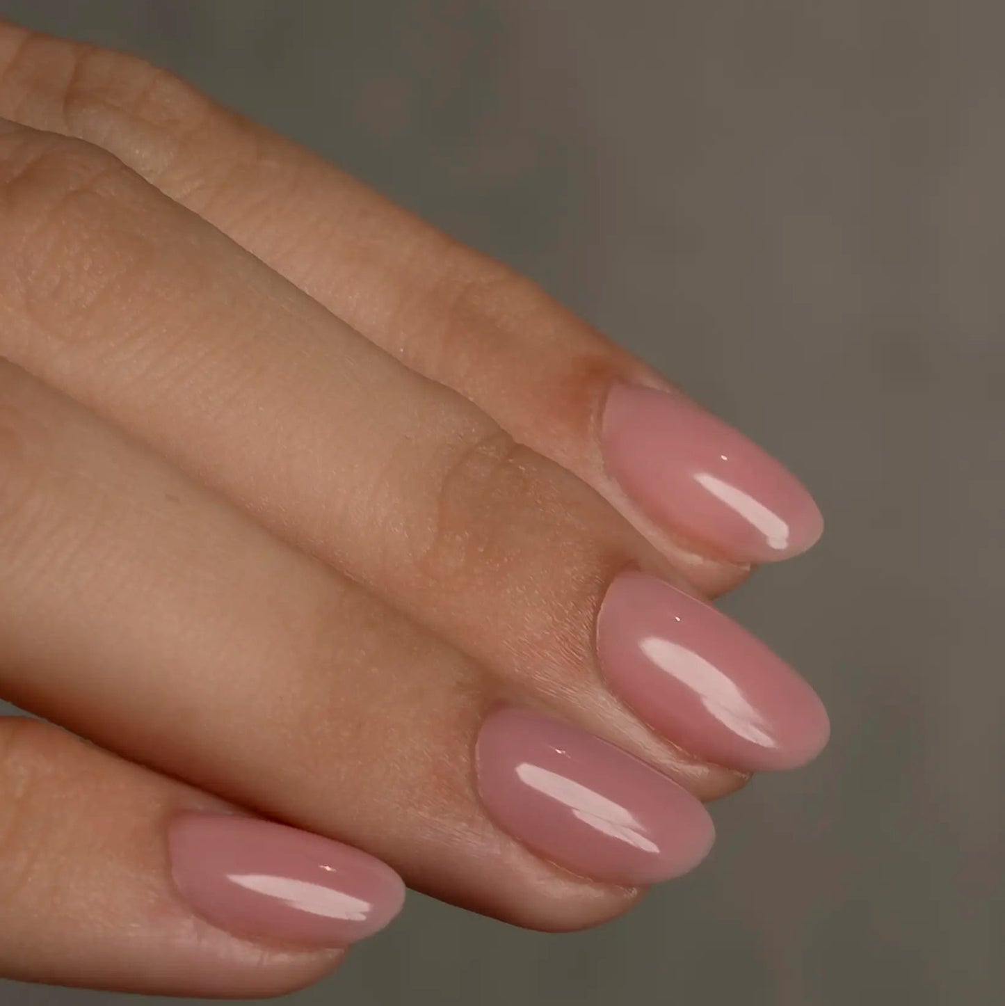 Close-up of a hand with pink nail polish on a neutral background