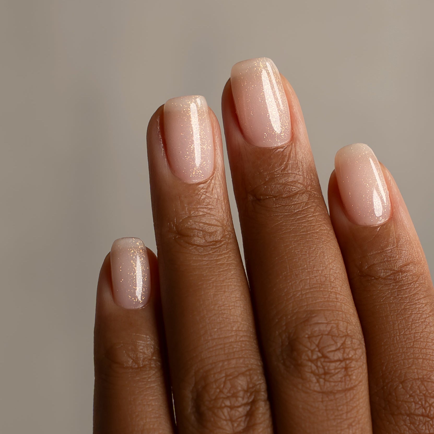 Close-up of a hand with beige nail polish on a neutral background