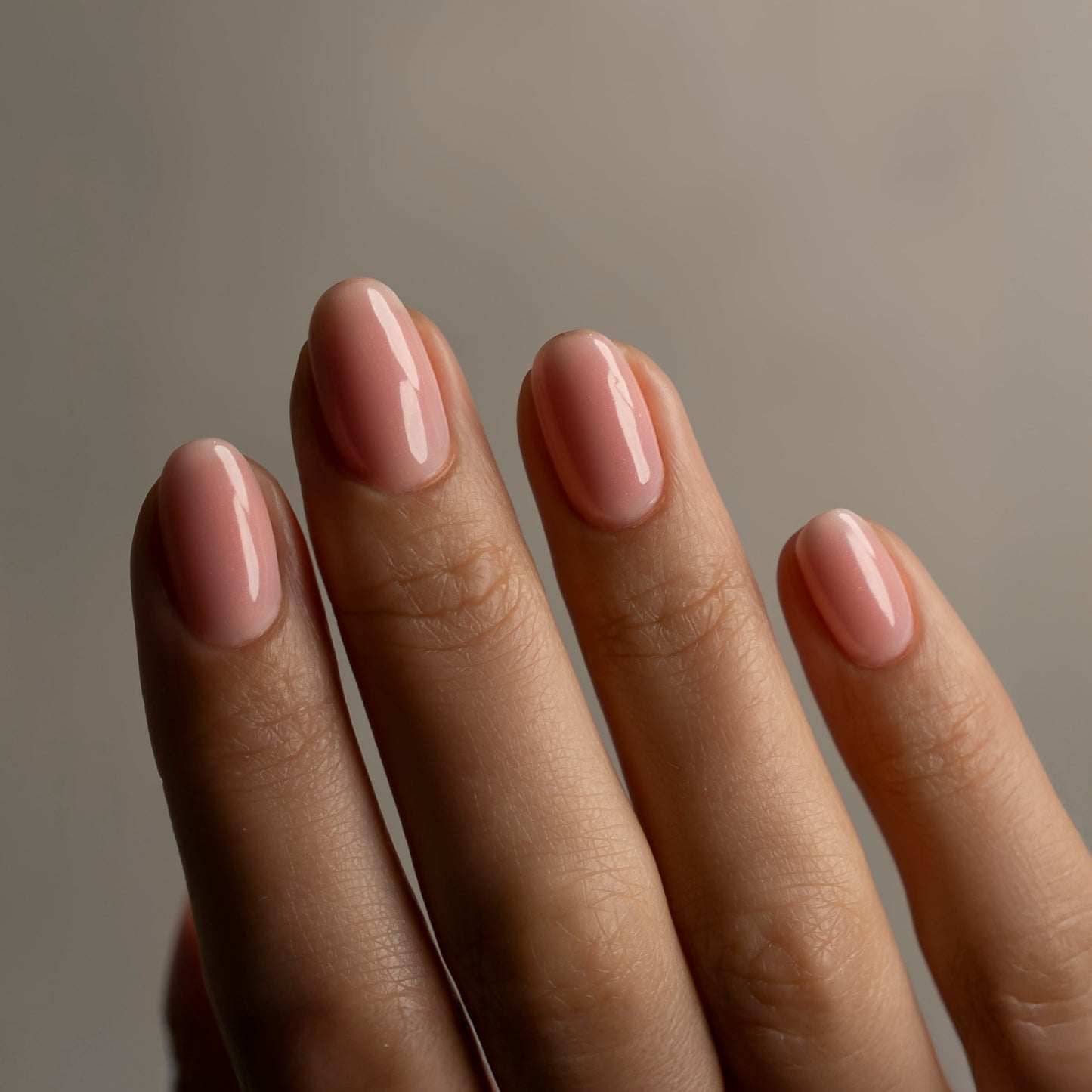 Close-up of a hand with pink nail polish against a neutral background