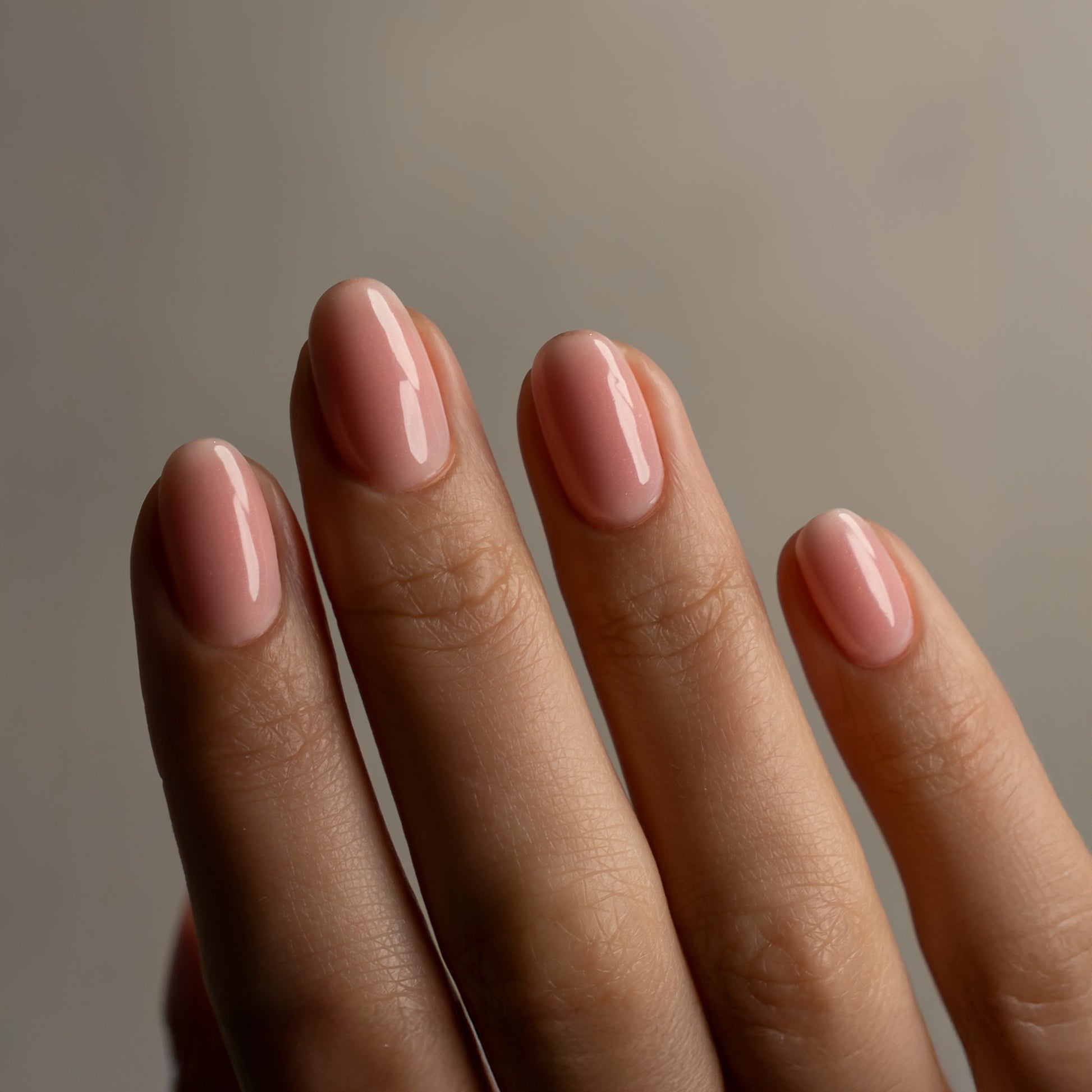 Close-up of a hand with pink nail polish against a neutral background