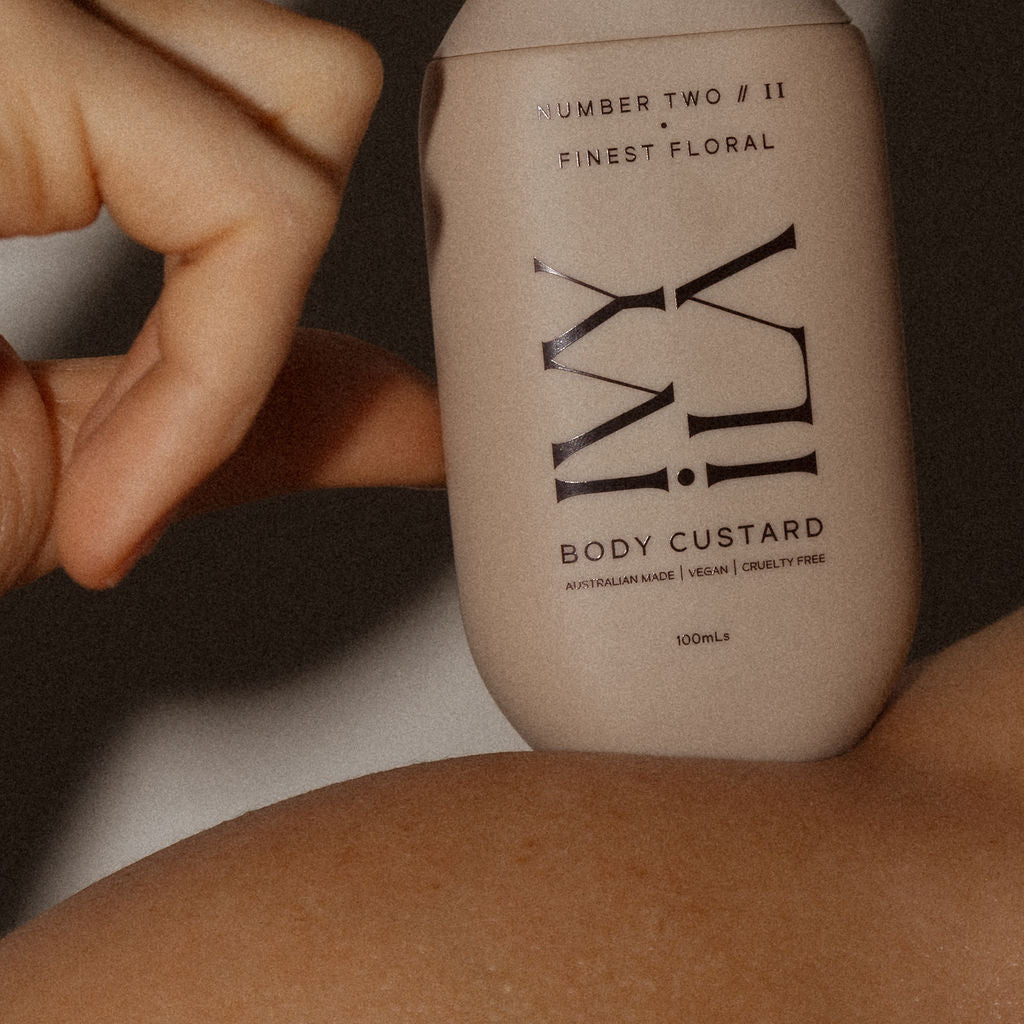 Hand holding a bottle of 'Ivy Ila' body custard against a blurred background