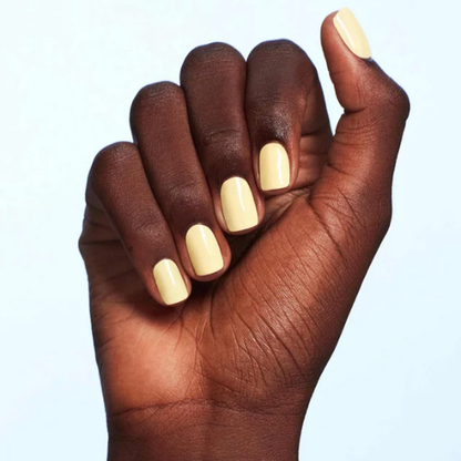 A close-up of a hand with a glossy pale yellow manicure against a light blue background.