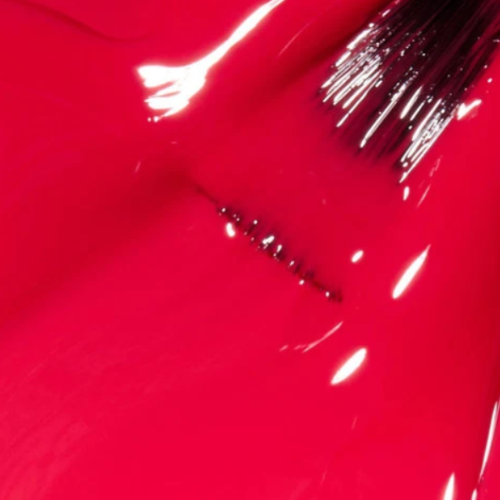 A close-up of glossy bright pink nail polish with a brush stroke and a thin painted line showing the color and finish.