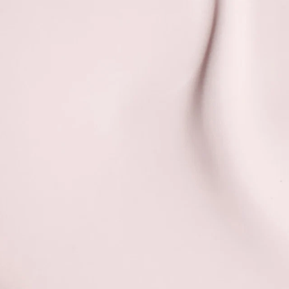 A close-up of a smooth, pale blush pink surface with soft shadows and a subtle curved highlight.