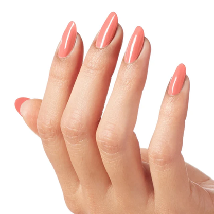 A close-up of a hand with long, almond-shaped nails painted in a glossy, solid coral pink shade, set against a plain white background.